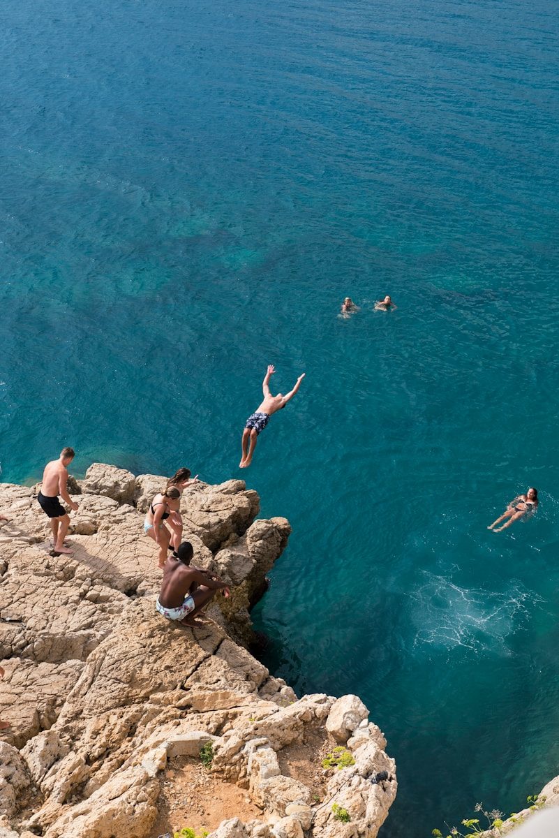 A man dives from a cliff into the turquoise sea.